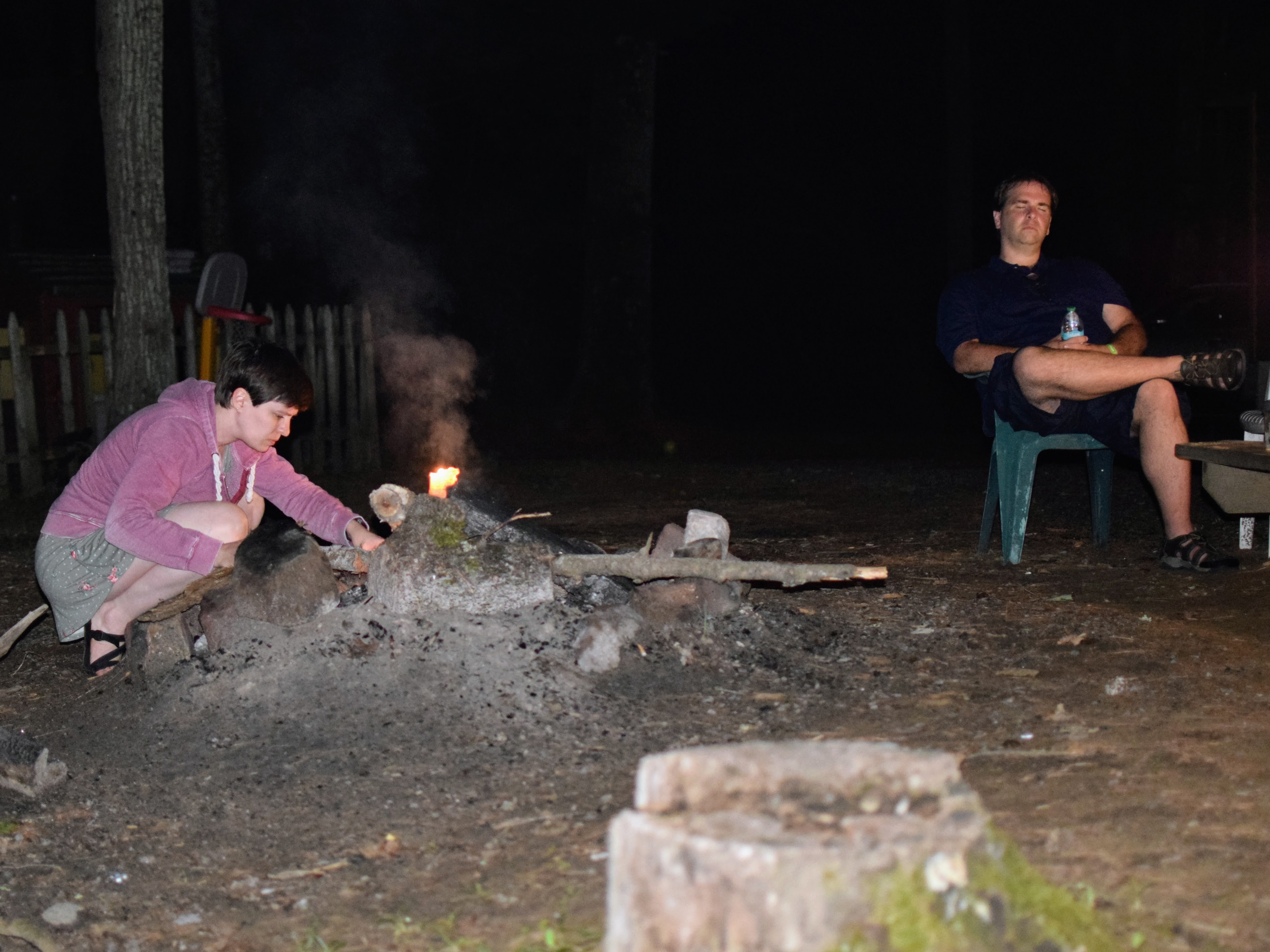 Amber building a small campfire. Bryan sits with eyes closed.