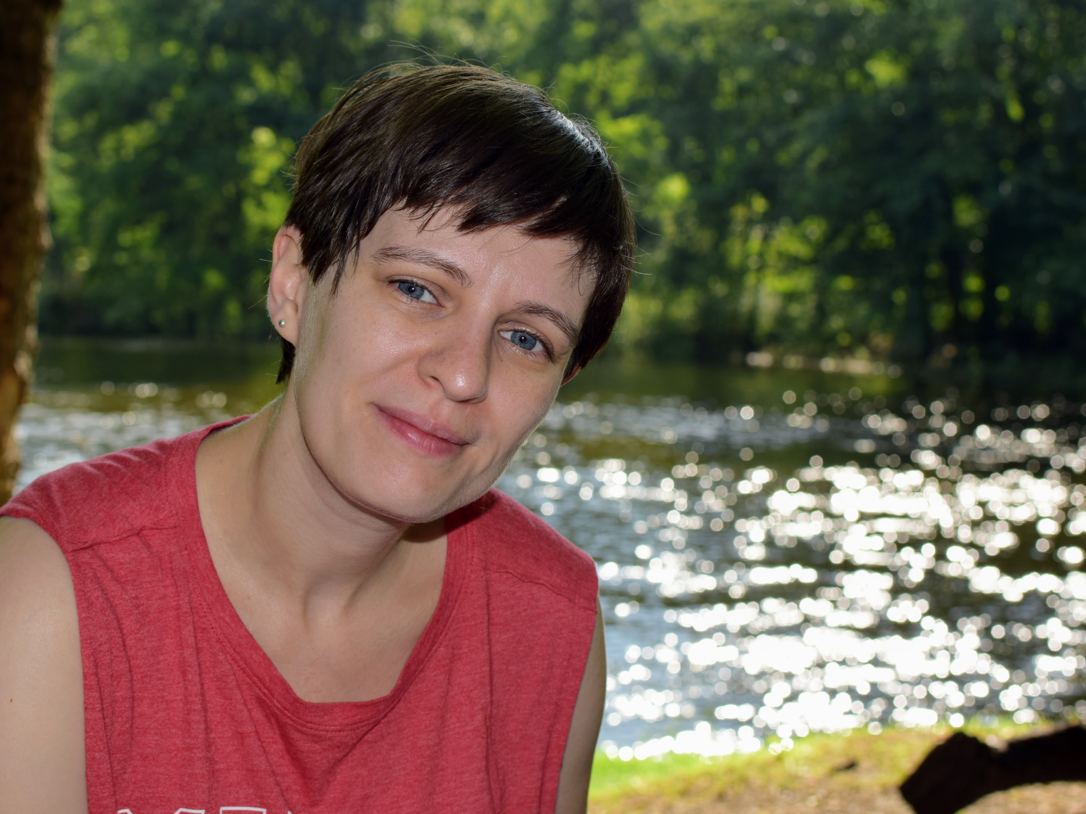 A short-haired femme person in front of a sparkling river