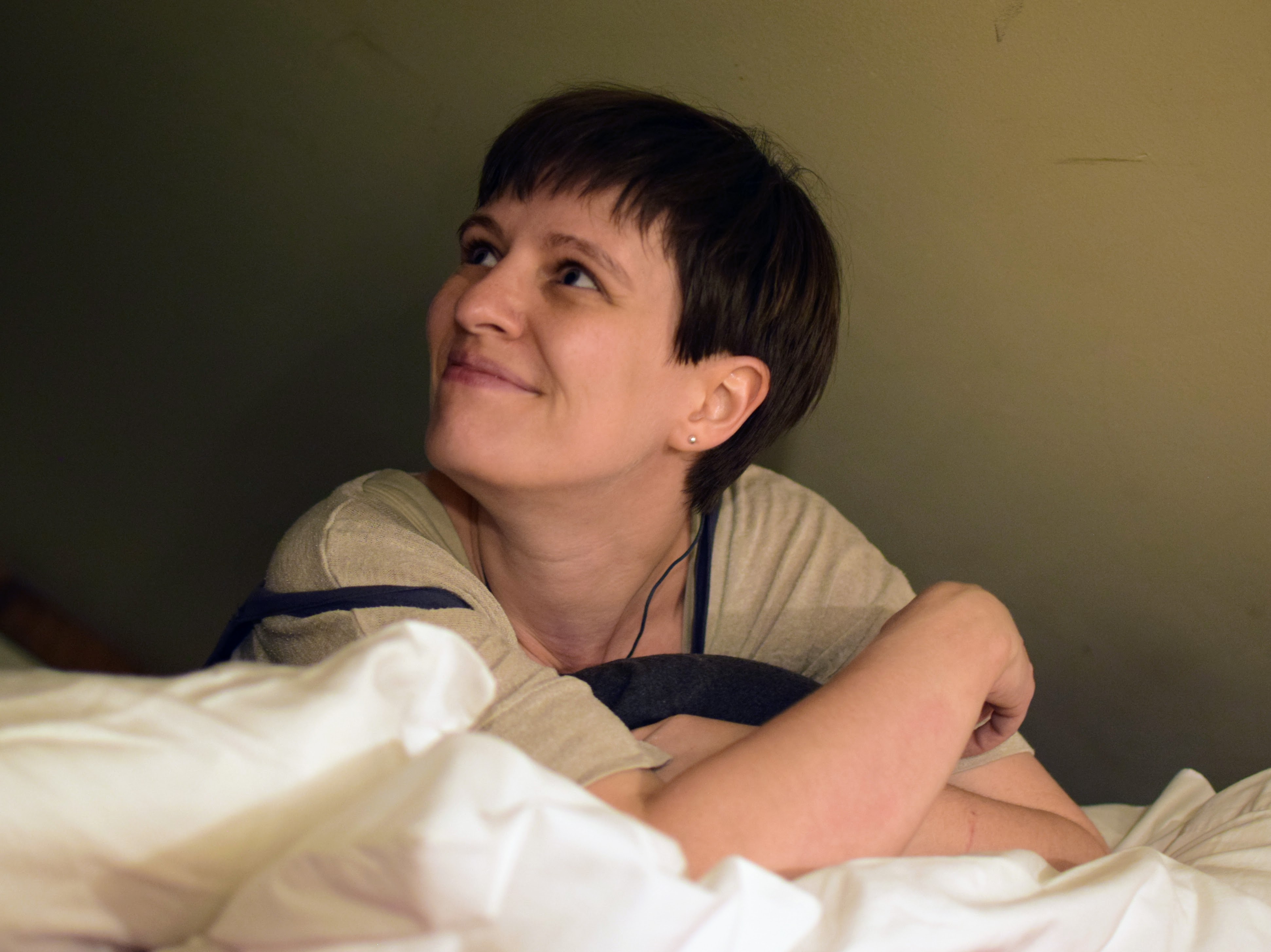 A feminine nonbinary person in a loft, looking to the left, smiling slightly