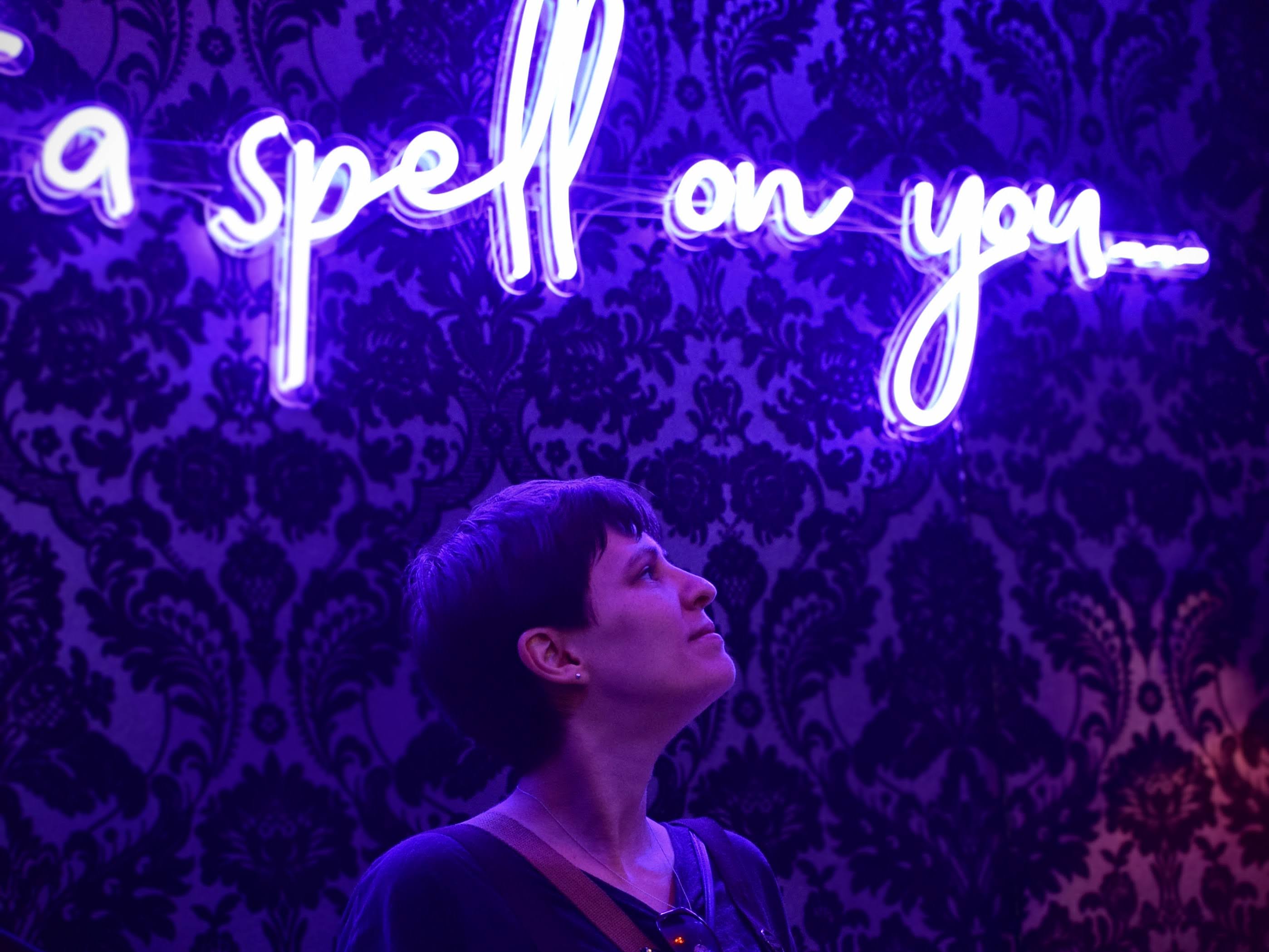 Amber looking up at a purple neon sign reading 'I put a spell on you'