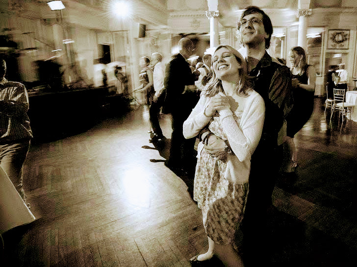 A monochrome picture of a couple dancing, the feminine one with their hands clutched before their chest