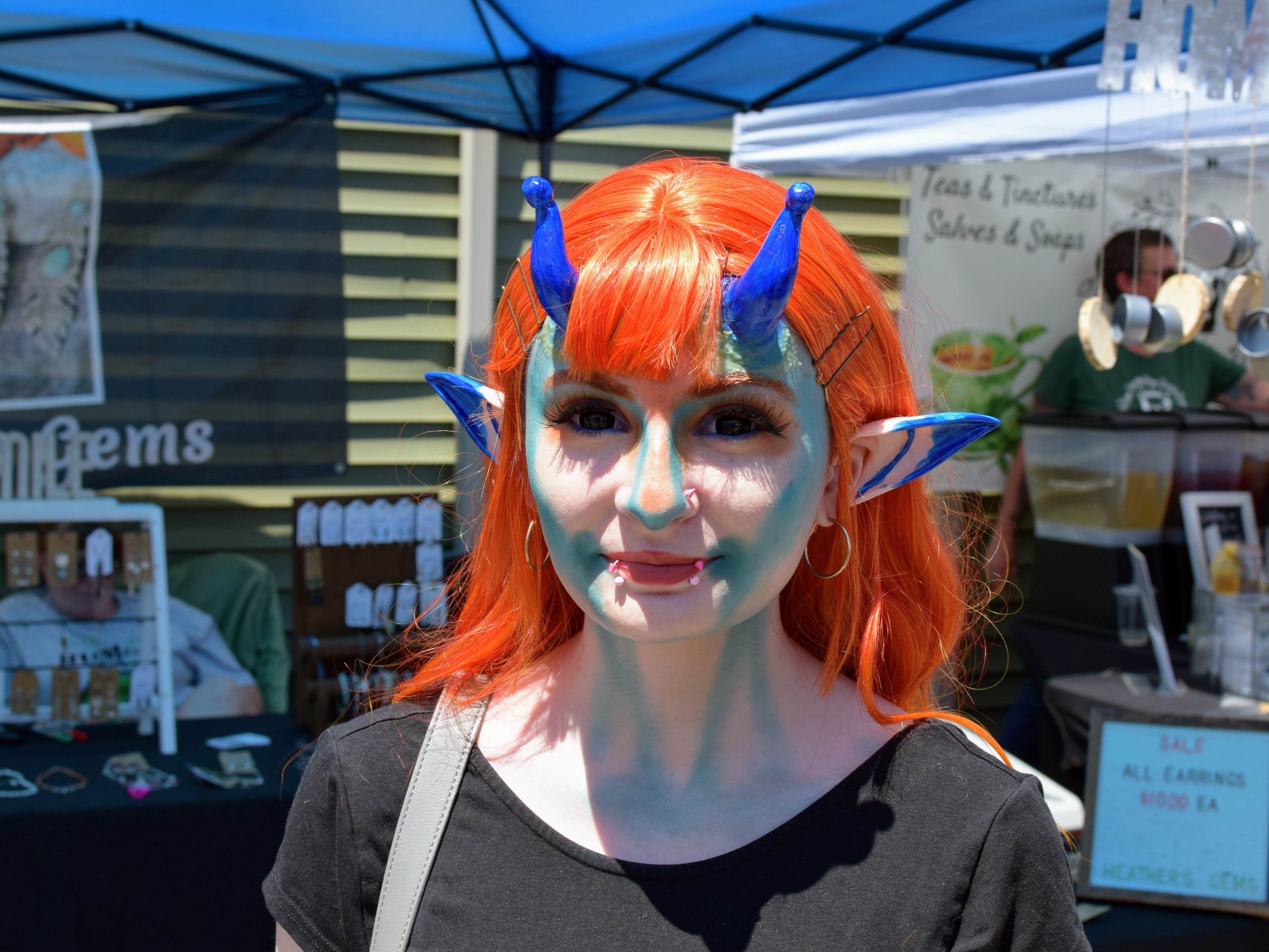 A woman dressed as an alien with blue face paint, horns, and orange hair