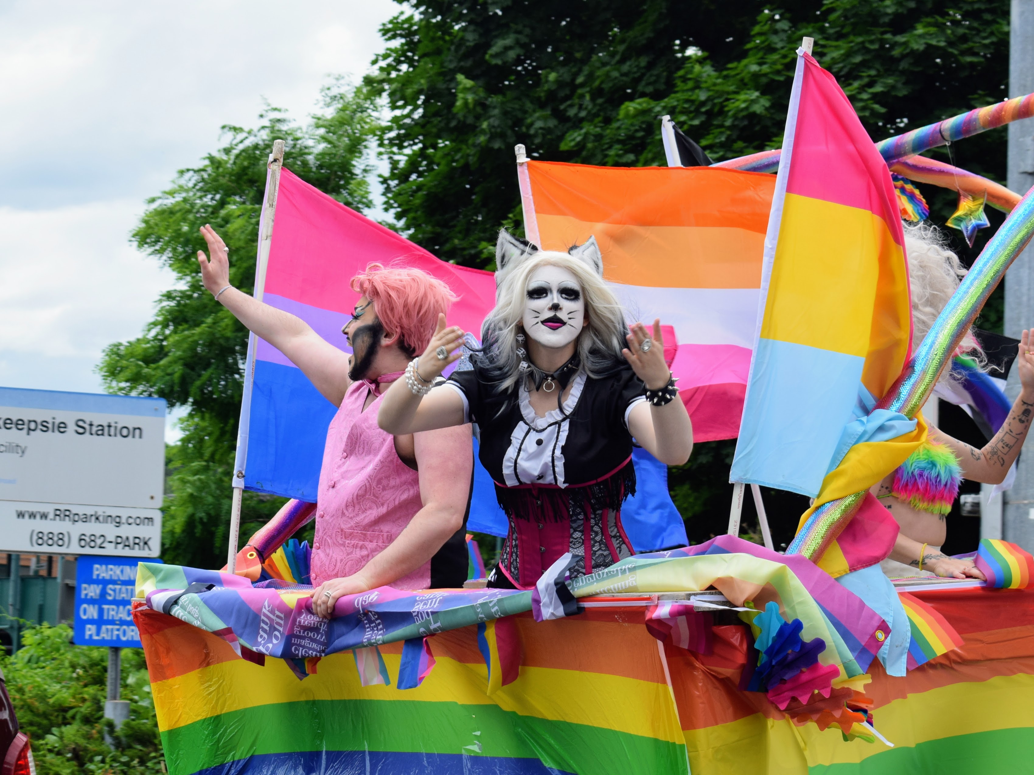 A drag queen on a float wearing cat makeup with Pride flags behind them