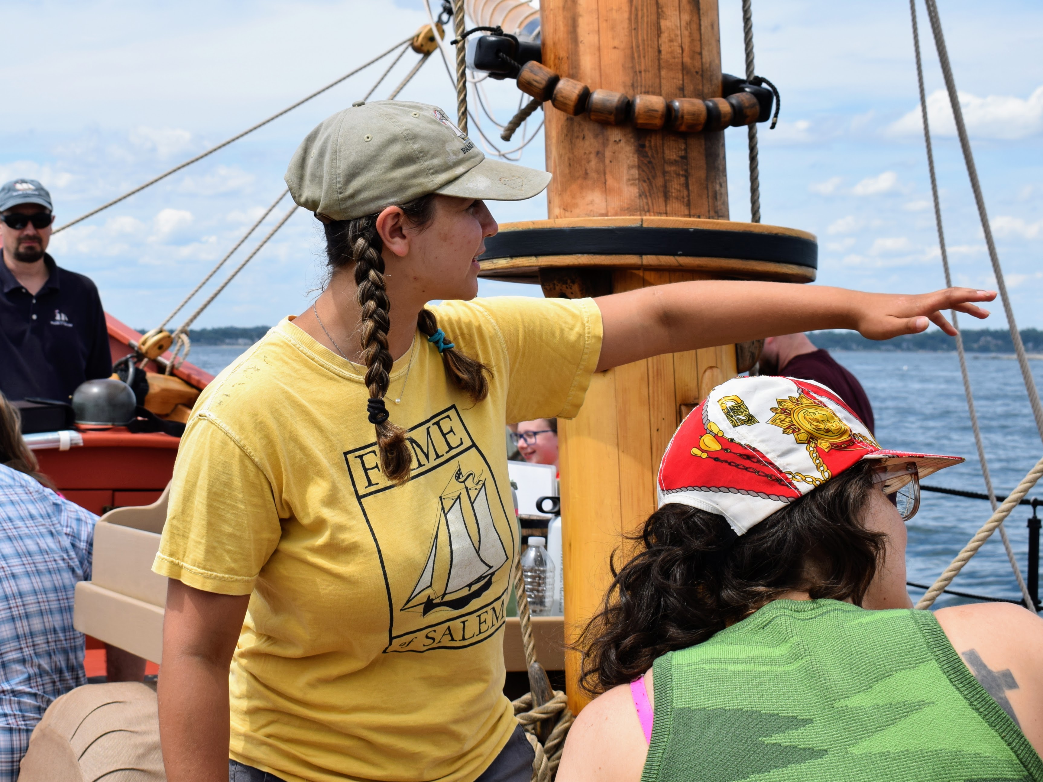 A young woman with braids in a tan hat and yellow shirt, pointing to the right