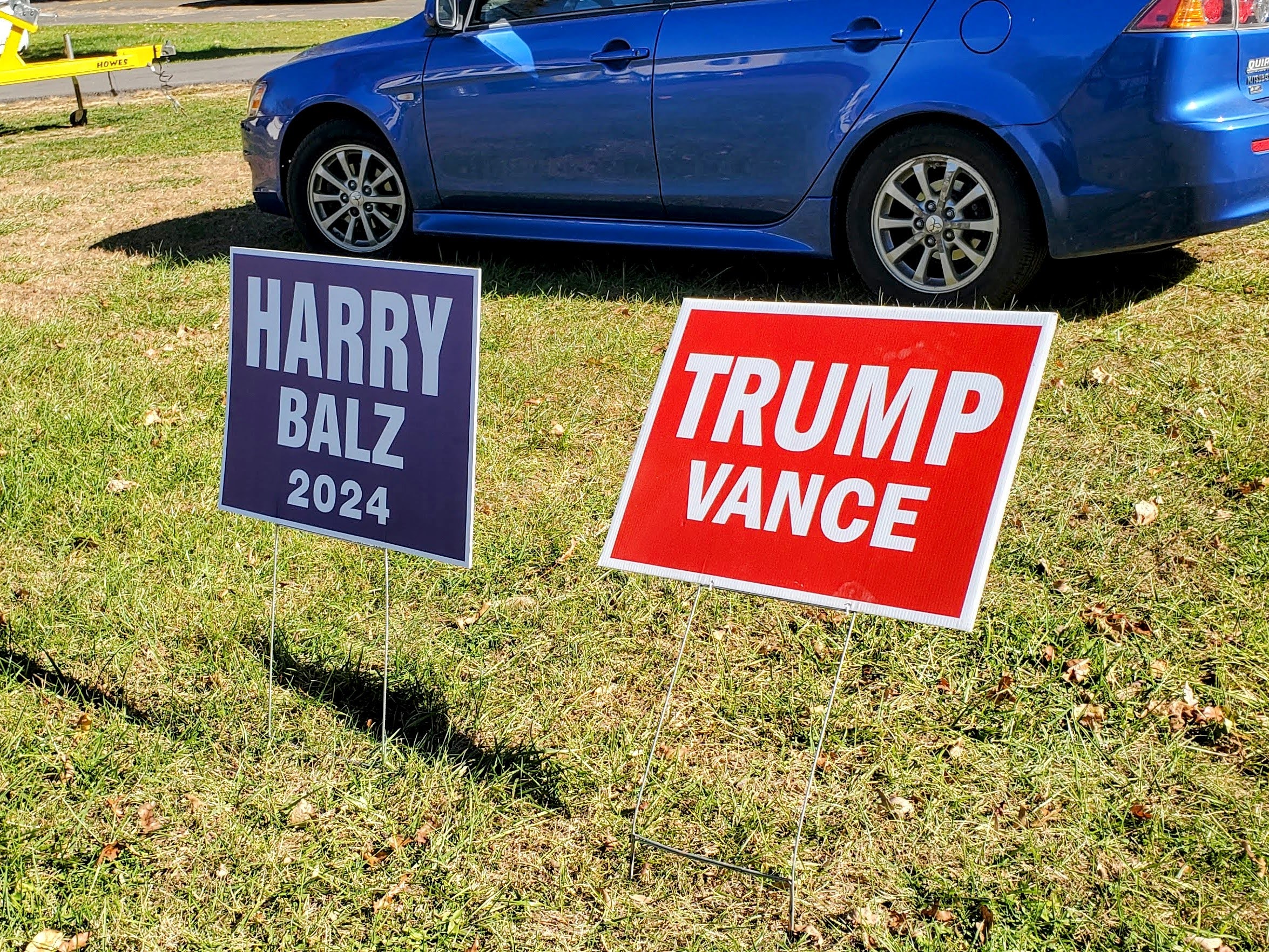 A blue political yard sign reading 'Harry Balz 2024' and a red one reading 'Trump Pence 2024'