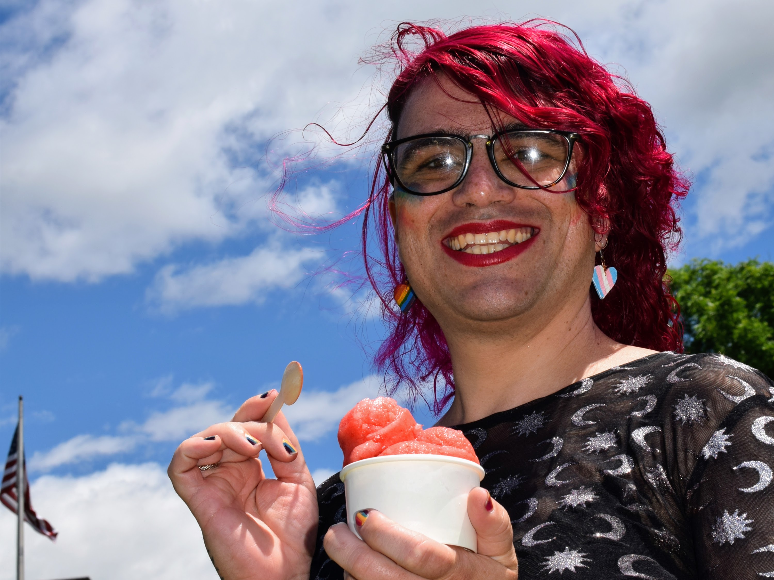 A person with red hair eating red Italian ice in front of a blue sky