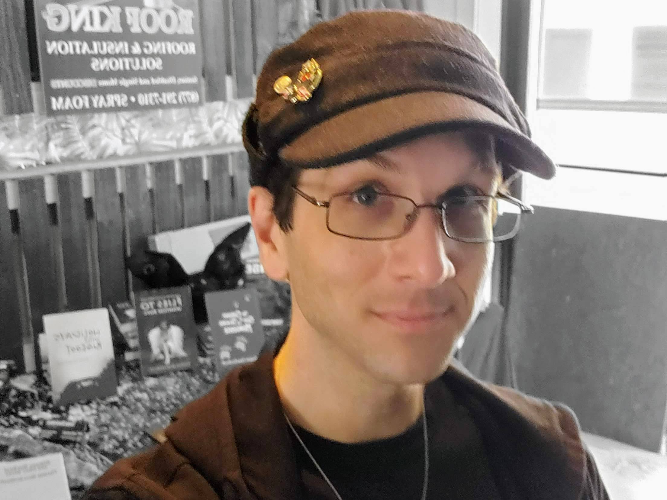 Man with glasses and a hat in front of books